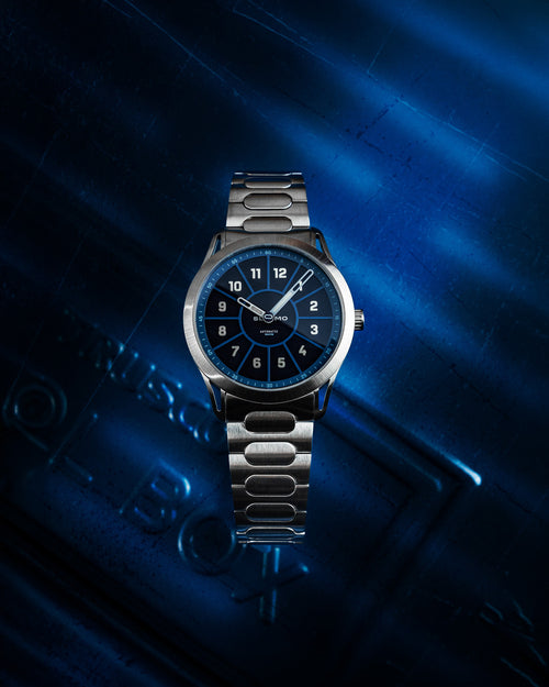 SLOMO Watches Glance automatic watch featuring a blue dial, white Arabic numerals, and a brushed steel bracelet. 