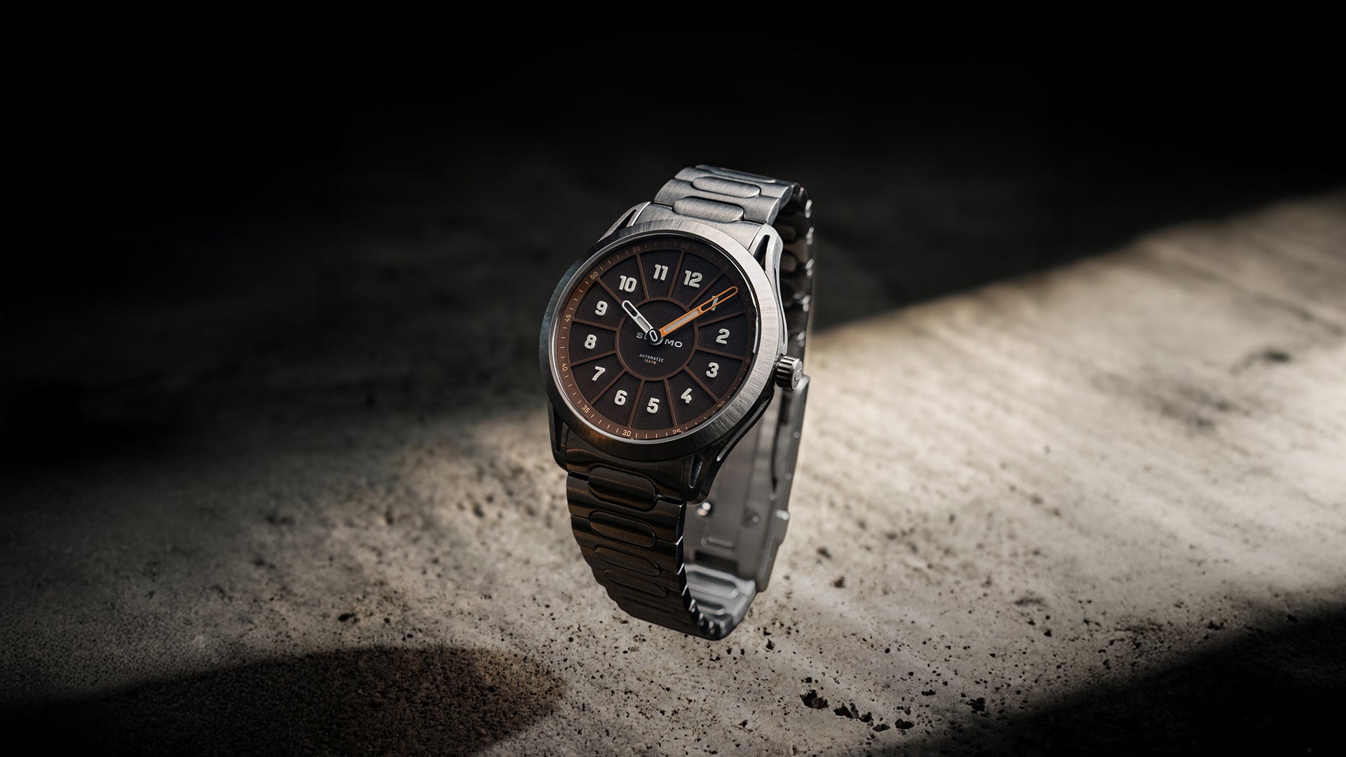 SLOMO Watches Glance automatic watch featuring a brown dial, white Arabic numerals, orange hands, and a brushed steel bracelet.