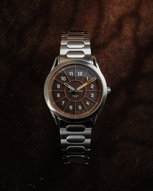 SLOMO Watches Glance automatic watch featuring a brown dial, white Arabic numerals, and a brushed steel bracelet. 
