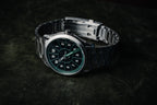 SLOMO Watches Glance automatic watch featuring a green dial, white Arabic numerals, and brushed steel bracelet resting with the clasp visible.