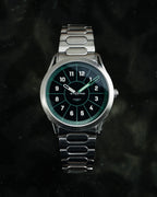 SLOMO Watches Glance automatic watch featuring a green dial, white Arabic numerals, and a brushed steel bracelet. 