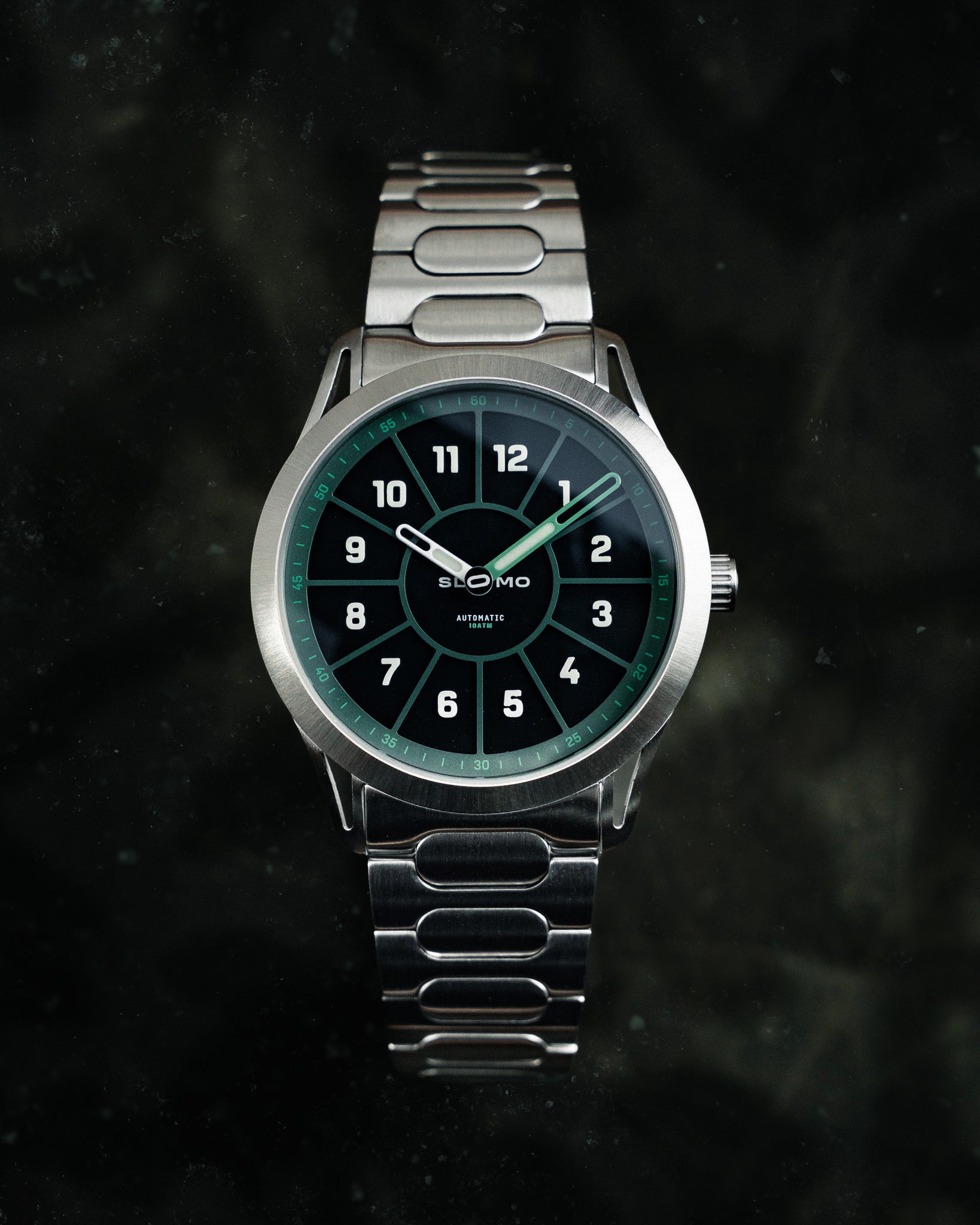 SLOMO Watches Glance automatic watch featuring a green dial, white Arabic numerals, and a brushed steel bracelet. 