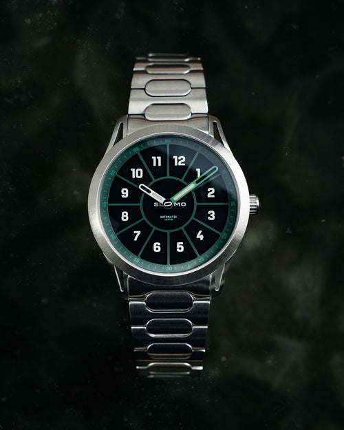 SLOMO Watches Glance automatic watch featuring a green dial, white Arabic numerals, and a brushed steel bracelet. 